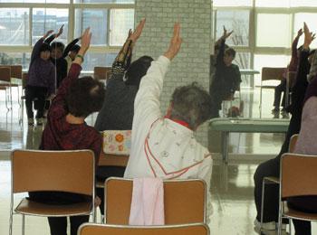 椅子に座りながら体操をしている参加者の写真