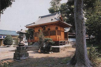 一本の木と石灯籠の間に見える瓦屋根にオレンジ色の外壁の雷伝神社の外観写真
