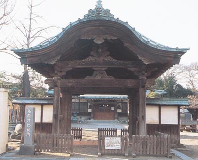 山型の屋根で木造の門構え、梁に彫刻が施された聖福寺勅使門（市指定有形文化財）の写真