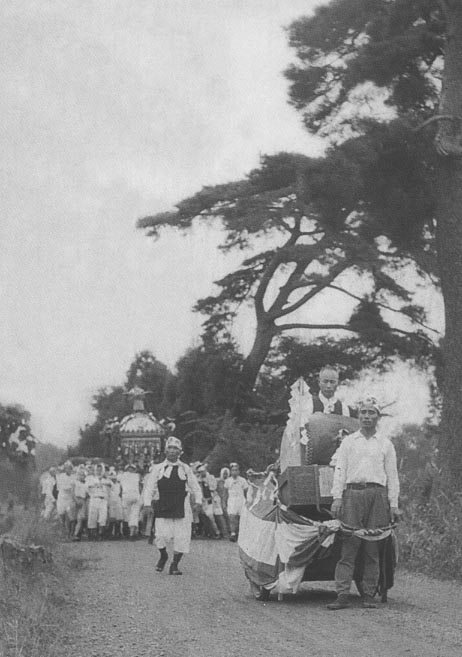 男性と太鼓を乗せたリヤカーを引いている男性、みこしを担いている男性が写っている八坂神社の夏祭りの白黒写真