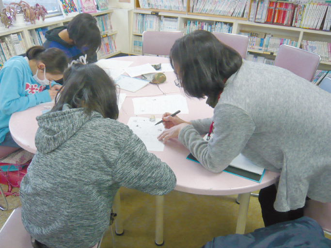 一つのテーブルに集まって3人の子供たちと先生が一緒に宿題をしている写真